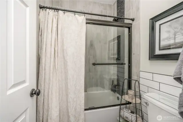 A shower/bath combo unit with glass doors and a window for natural light but high enough for privacy.