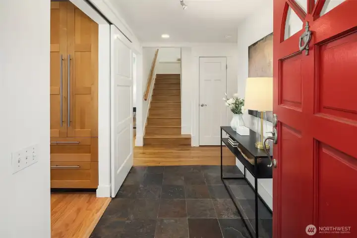 A vibrant red entry door opens to warm hardwoods, slate flooring, and clean architectural lines — creating a bright, welcoming sense of arrival.