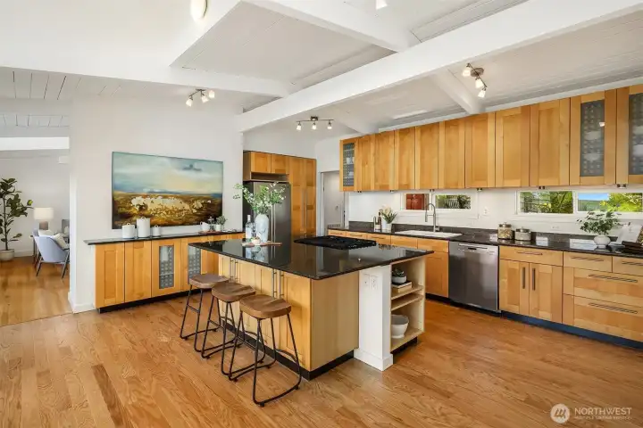 Vaulted ceilings and warm wood cabinetry bring character and scale to the open-concept kitchen, complete with expansive prep space, abundant storage, and effortless connection to the surrounding living and dining areas.