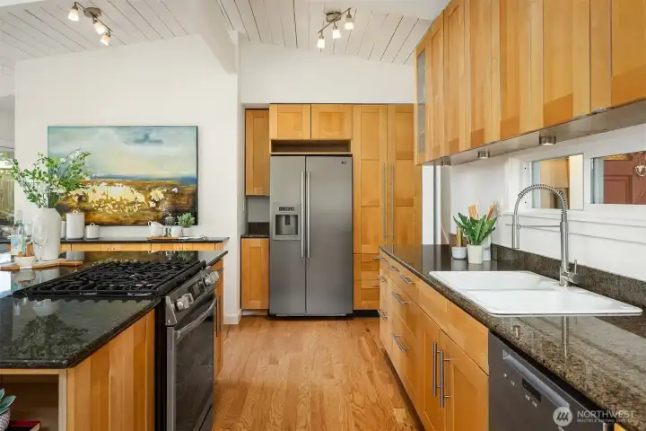 Clean-lined wood cabinetry, generous counter space, and an oversized island with integrated cooktop create a warm, functional kitchen designed for gathering, cooking, and effortless everyday living.