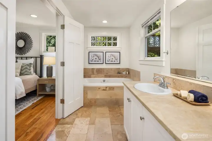 The ensuite bath is finished in warm travertine stone and features a jetted soaking tub, generous vanity, and a calming spa-like atmosphere designed for everyday retreat.