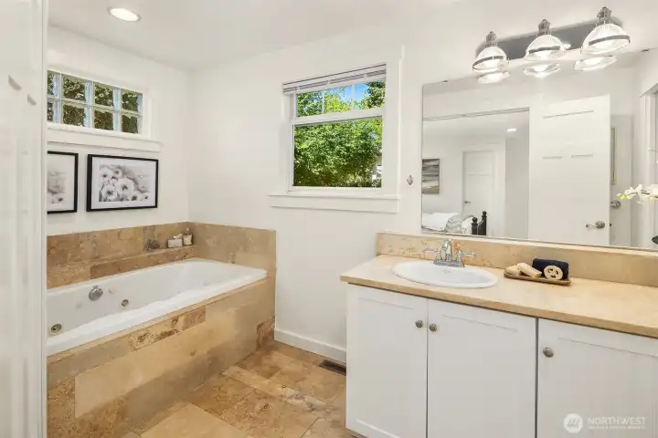 The ensuite bath is finished in warm travertine stone and features a jetted soaking tub, generous vanity, and a calming spa-like atmosphere designed for everyday retreat.