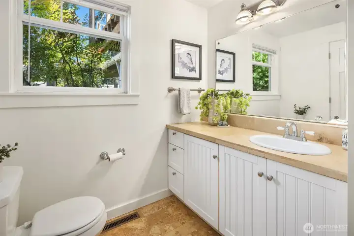 The main-floor bath pairs clean white millwork with warm stone finishes and includes a shower for comfortable everyday living and guest convenience.