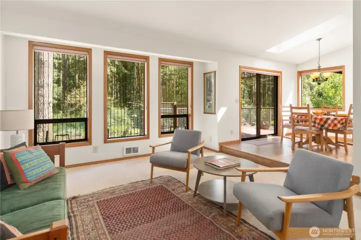 Large living room with windows looking out to the back yard and the woods beyond.