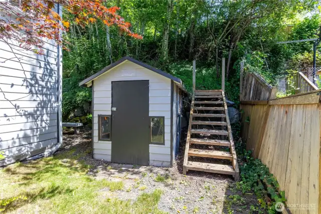 Outbuilding on the south side of house has windows and locking door. Stairs are for people or pets to access the upper yard and fence if needed. Yard behind this photo would be great for garden boxes, garbage can storage, or even for some recreational toys.