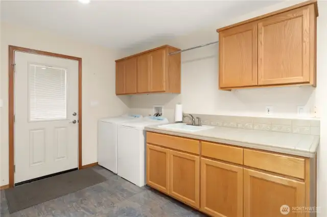 Very large laundry room with a door leading outside. There is a bar for hanging clothes and a utility sink.