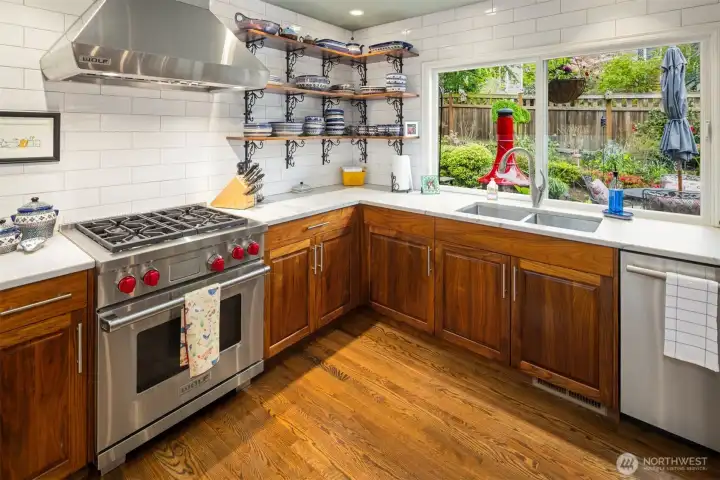Kitchen features stainless steel appliances, including a large Sub-Zero refrigerator and a professional-style Wolf range with a hood. The backsplash is made of white subway tile, and open wooden shelves display dishes and decor.