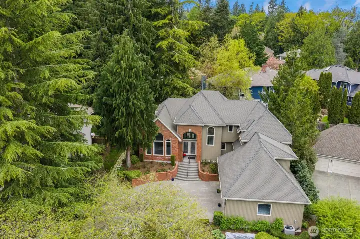 Large, multi-level residence with a combination of brick and neutral-toned siding, topped by a gray, multi-gabled roof. A prominent front entry sits at the top of a short set of curved steps, framed by a brick façade and tall windows that bring in natural light.