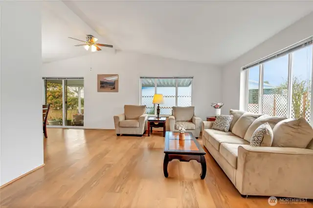 Large living room with new beautiful laminate waterproof hardwood flooring. Big windows flood the living areas with natural light. Tall vaulted ceiling with fan. Notice the pretty new lattice work outside the windows for extra privacy around the backyard area.