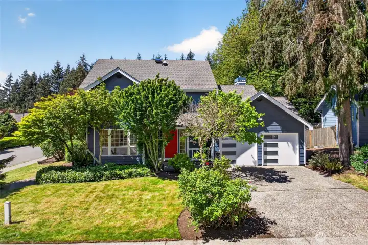 Sunlit and surrounded by lush, established greenery, the home presents beautifully from the street with its classic Pacific Northwest architecture and inviting front porch. A generous lawn, layered shrubs, and that crisp red door create a welcoming first impression rare to find in this part of English Hill.