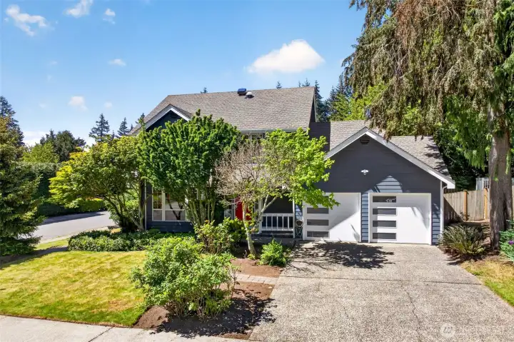 A wider angle reveals the home's depth and the privacy afforded by towering evergreens along the property line, creating a peaceful, tucked-away feel just minutes from Redmond's tech corridor. The contemporary garage doors installed in 2025 add a refined modern note to the home's enduring Northwest character.