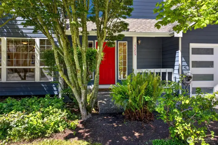 The covered entry welcomes guests with charm and personality, framed by graceful Japanese maples and layered ferns that thrive in the Pacific Northwest climate. Crisp white trim, the bold red door, and clean address numerals signal pride of ownership the moment you arrive.