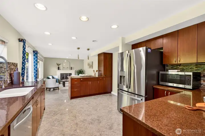 A wider look at the kitchen reveals the smart, open layout connecting cooking, dining, and the cozy family room with white brick gas fireplace just beyond. Granite tile floors, stainless appliances, and updated dimmable lighting deliver everyday function with elevated style.