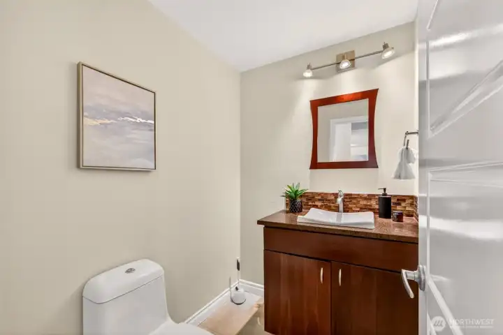 The convenient main-floor powder room continues the home's elevated design with custom dark cabinetry, a sleek vessel sink, and stone tile backsplash that ties beautifully to the kitchen finishes. Thoughtful track lighting adds a modern, hospitality-inspired touch perfect for greeting guests.