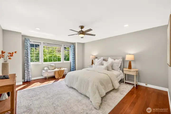 The spacious primary suite enjoys leafy treetop views through a wide picture window and stays serene thanks to a quiet ceiling fan and updated wafer LED lighting. Rich hardwood floors continue throughout the upper level, while a custom modular closet system keeps wardrobe organization effortless.