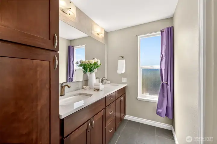 The primary bath delivers everyday luxury with a double vanity, quartz counters, and custom dark cabinetry that ties beautifully to the kitchen finishes. Two sinks mean no more morning traffic jams, while a privacy window keeps the space bright without sacrificing seclusion.