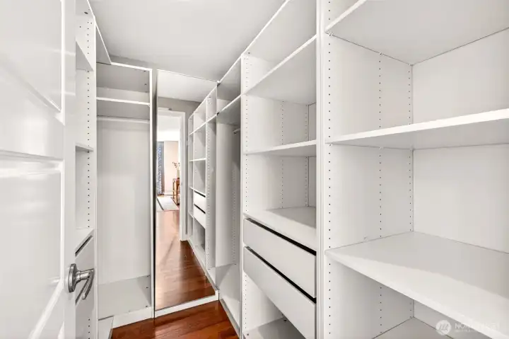 The walk-in primary closet features a custom modular storage system with adjustable shelving, drawers, and hanging rods designed to grow with your wardrobe. Mirrored details and rich hardwood floors give this everyday space a tailored, boutique-shop feel.
