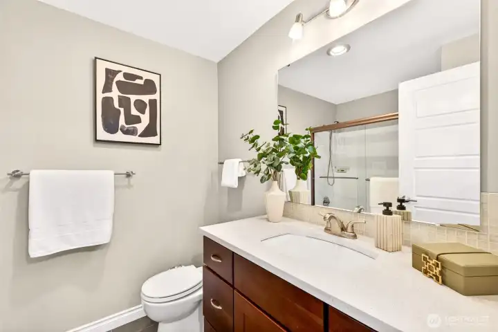 The upper-level hall bath continues the home's elevated design with quartz counters, custom dark cabinetry, and a walk-in shower behind sleek glass doors. Updated tile flooring and modern fixtures bring this everyday space well into the current decade.