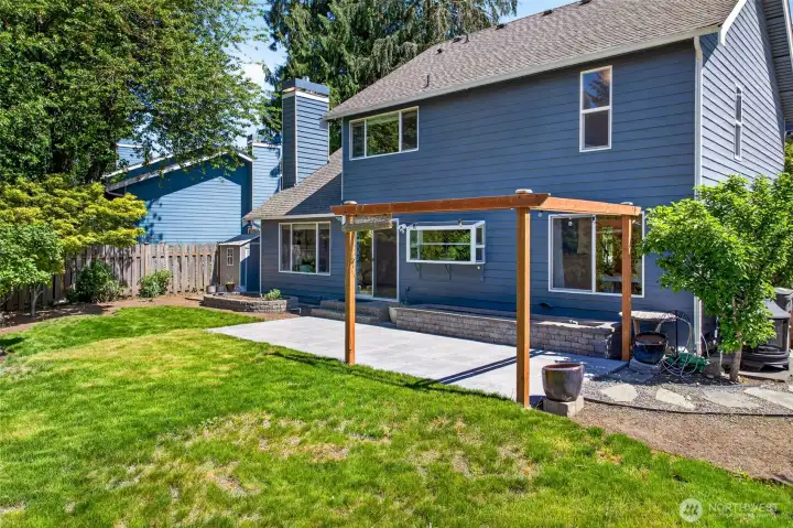 The home's rear elevation reveals the thoughtful blend of architecture and landscape, with the cedar pergola anchoring the patio and the garden window above the kitchen sink bringing the outdoors in. Updated vinyl windows, classic Northwest siding, and a private fenced yard make this a low-maintenance retreat ready to enjoy from day one.