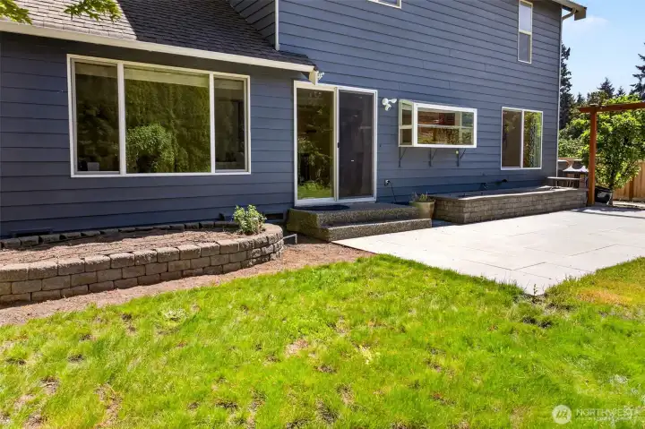 A closer view of the patio area reveals the convenient slider connecting the dining room directly to the outdoor living space, perfect for effortless indoor-outdoor flow during gatherings. Raised stone planters provide built-in opportunities for seasonal flowers, vegetables, or herbs just steps from the kitchen.