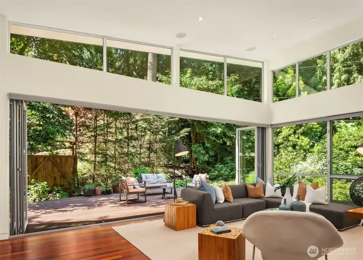 With both folding glass walls open, the great room and deck function as a single indoor-outdoor living space. Clerestory windows wrap the room, pulling in filtered light and treetop views.