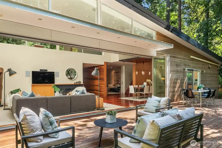 From the deck, the open glass walls reveal the full main level — living, dining, and kitchen — designed for entertaining inside and out at once.