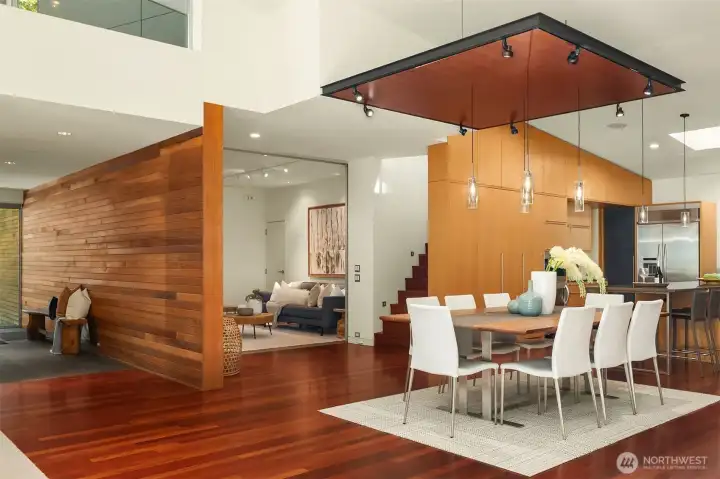 The cedar-clad entry gallery and floating hearth wall organize the main level, with the dining area set beneath a suspended wood ceiling panel with integrated track lighting.