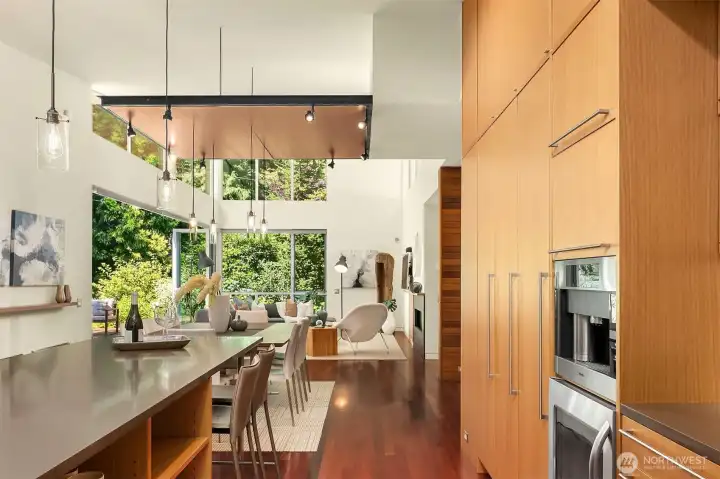 The kitchen's long island and cabinet wall look straight through the dining area to the living room and gardens beyond.