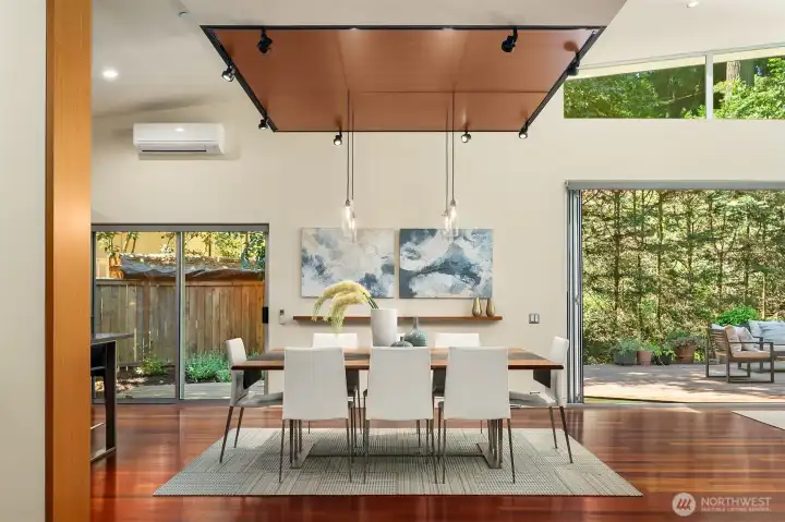 The dining area sits at the crossroads of the plan — deck on one side, side garden on the other — under pendant lighting and the suspended ceiling plane.