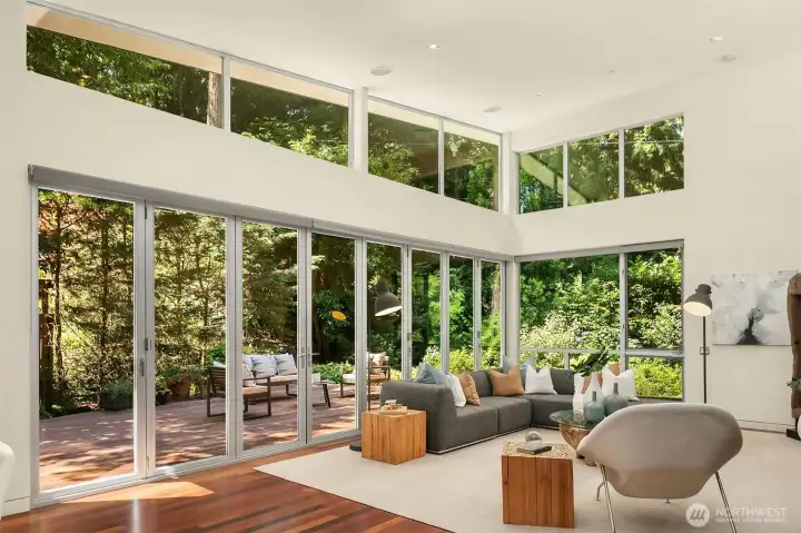 Even with the folding walls closed, the living room stays connected to the outdoors — two stories of glass on two sides, with the deck and gardens beyond.