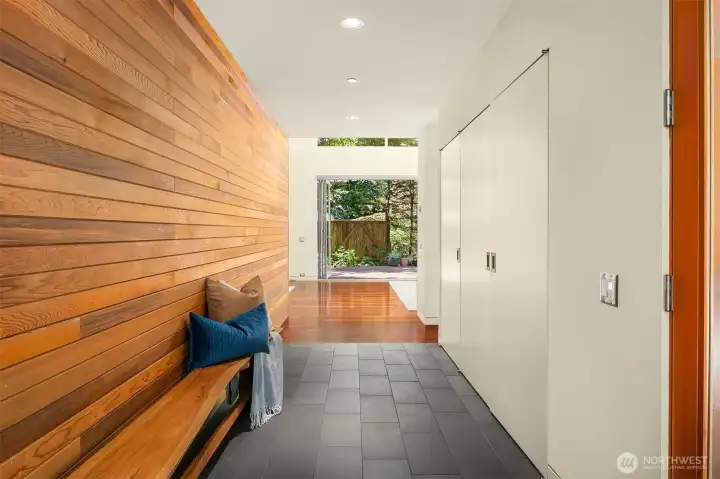 Inside the entry, a cedar-clad wall and built-in bench run the length of the gallery hall, with slate tile giving way to Brazilian cherry floors and a sightline straight through to the back deck.