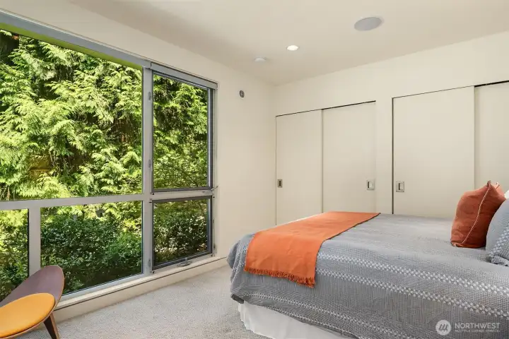 Main floor guest bedroom with a full wall of closets and windows framing the surrounding greenery.