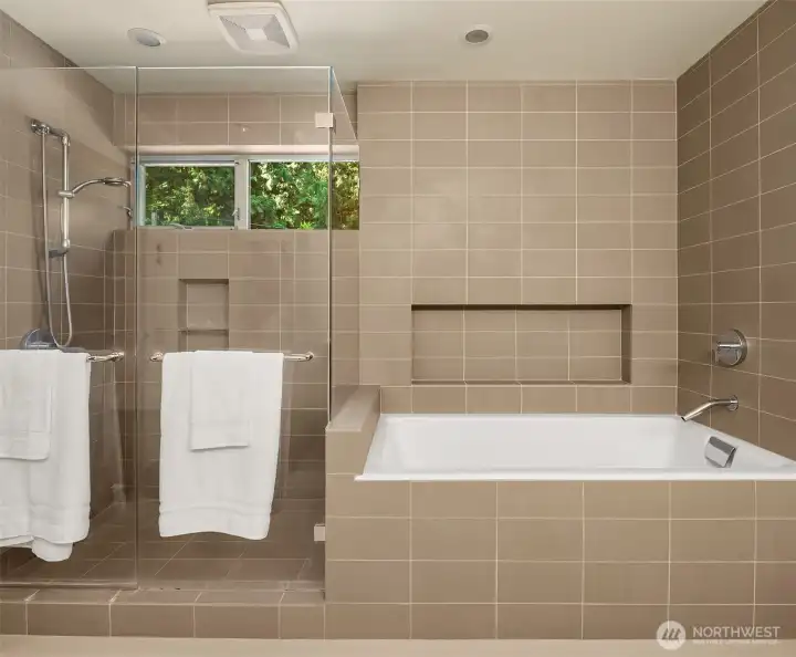 A frameless glass shower and separate soaking tub share a tiled wet zone, with a window set into the treetops.