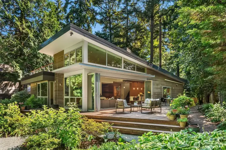 The rear elevation from the garden: two stories of glass under the shed roofline, with folding door walls opening the main level to the entertaining deck.