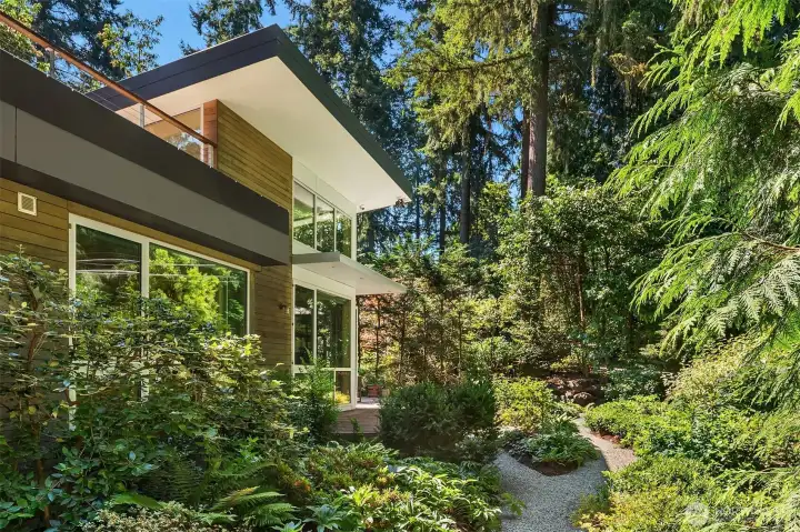 A gravel path traces the perimeter gardens, where layered ferns, rhododendrons, and evergreens create privacy on all sides.