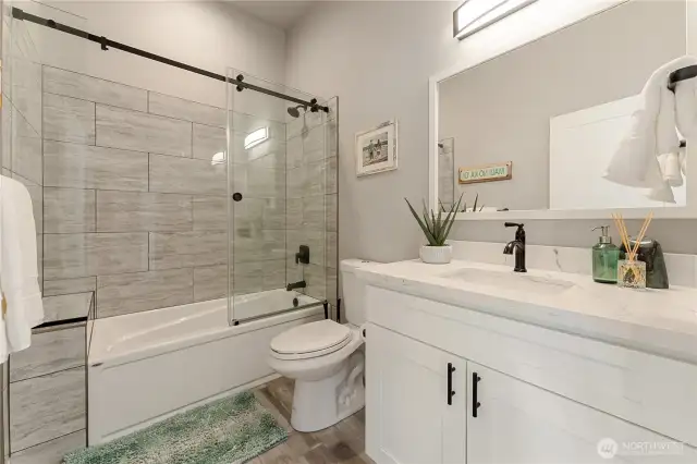 View of the upper level Guest Bathroom suite w/ quartz countertops & a frameless glass & tile shower.