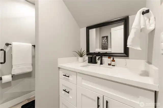 View of lower level bathroom w/ quartz countertops & a frameless glass & tile shower.