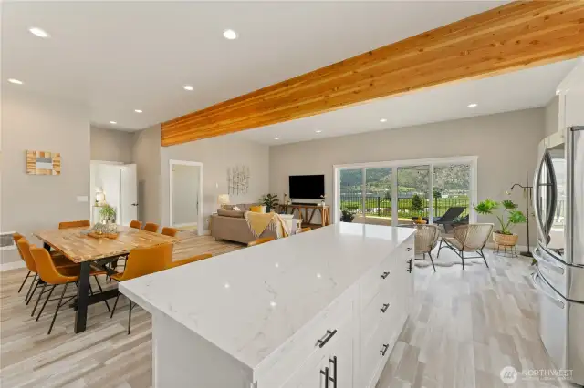 View 4 of kitchen w/ high-end appliances, quartz countertops & sit up bar looking towards the spacious dining room, living room & sitting room w/ sliding glass doors leading out to the large lake view deck.