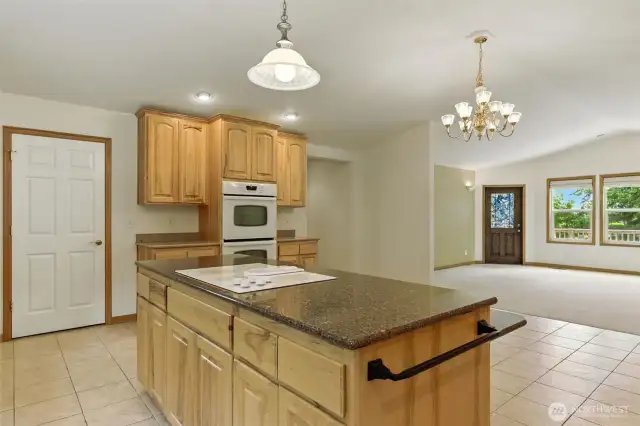 The island has a sleek electric cooktop and generous granite counter space, with a double oven conveniently located nearby for effortless meal prep