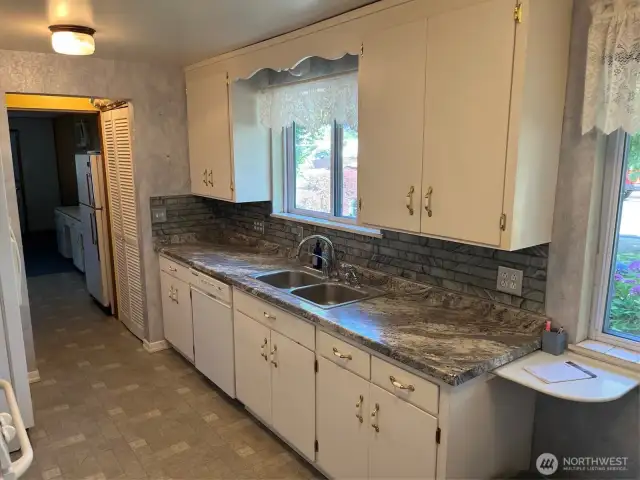 Right side of kitchen has sink dishwasher and Pantry in breezeway on both sides and around corner in Living room. New Counter and tiles. Lots of Cabinets for storage. Looks out to front gardens and driveway.