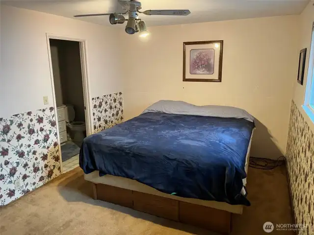 Primary Bedroom with 3/4 Bathroom. Floral Wallpaper and Ceiling Fan. Hardwood floors hidden under current tan carpet.
