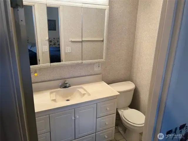 Primary Bathroom with Vanity medicine cabinet mirror with lights above, and Toilet and shower. Light grey wall paper for finished look.