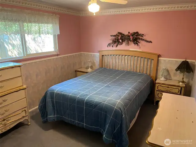 Second Bedroom with Pink paint above wallpaper and white trim below. Ceiling Fan and light blue carpet. Hidden under carpet is Hardwood Floors.
