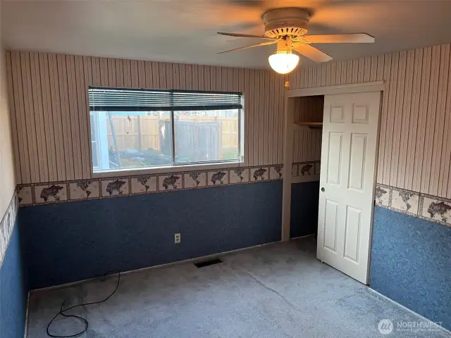 4th Bedroom at West end of house looks out to back yard. Has decorative wall paper and Ceiling Fan above.