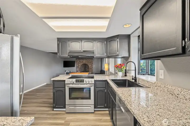 The updated kitchen boasts granite countertops, stainless steel appliances, and dark cabinetry for a modern contrast. An oversized sink and window brings in natural light and frames a beautiful treetop view.