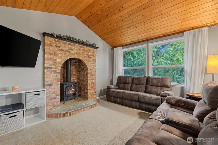 The cozy family room features a vaulted wood-paneled ceiling, large picture windows, and a brick hearth with a gas stove insert. The perfect blend of warmth and character!