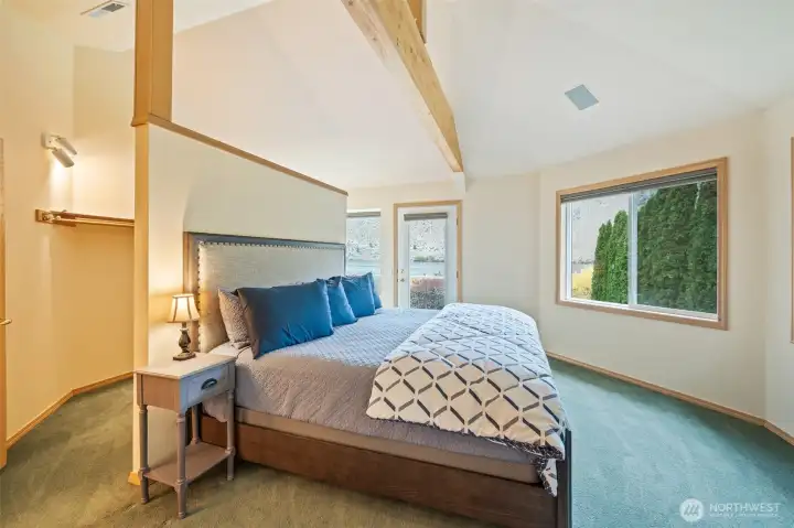 Warm and inviting primary suite with large windows, high ceilings, and direct entry to the walk-in closet and private balcony overlooking the river.