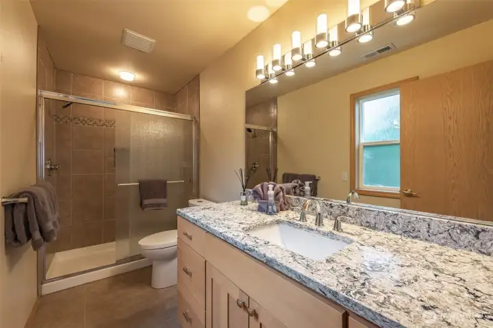 Updated primary bathroom with granite counters, double sink, modern lighting, and a large tiled shower with glass doors. Bright, clean, and designed for comfort.