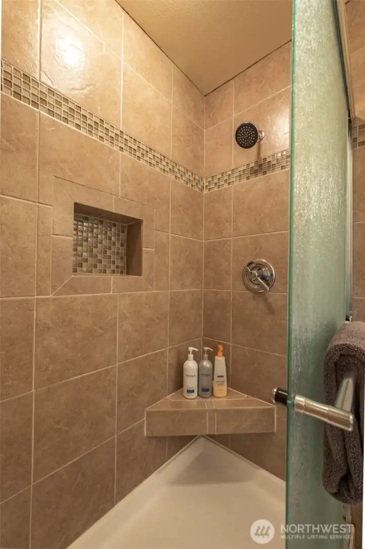 Beautifully tiled walk-in shower with glass door, built-in niches, and accent tile detailing — a clean, upgraded feature of the primary bathroom.