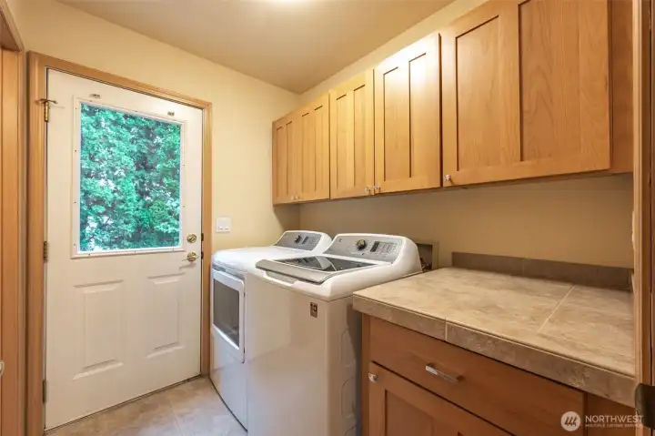 Dedicated laundry room with upper cabinetry, tile counters, and exterior access for added convenience.